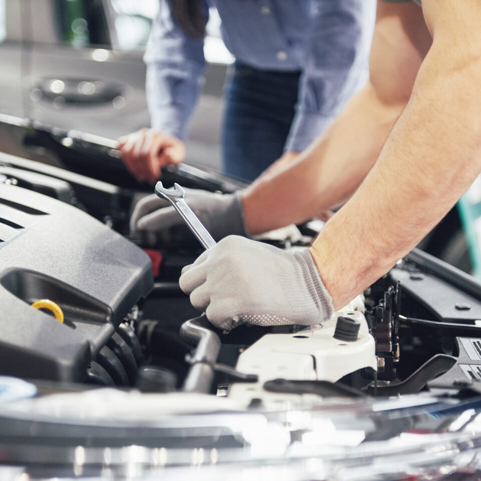 A man mechanic and woman customer look at the car hood and discuss repairs